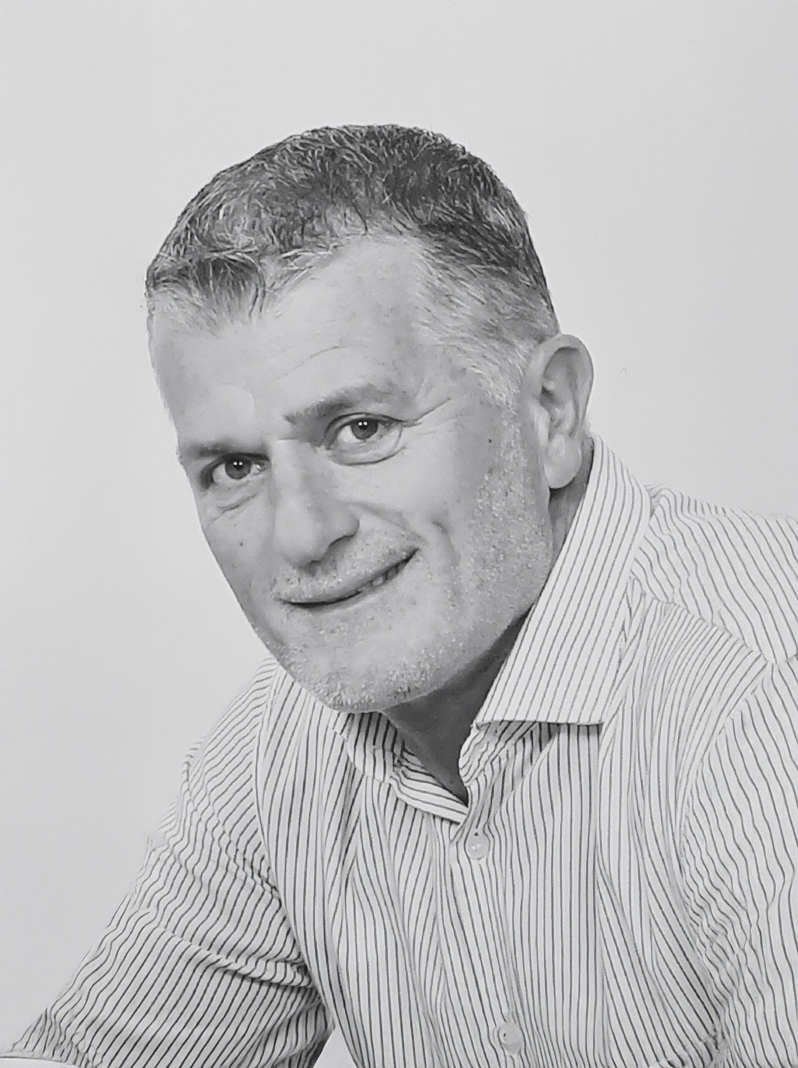 Homme mûr souriant vu en plan rapproché, cheveux courts poivre et sel, chemise rayée claire.