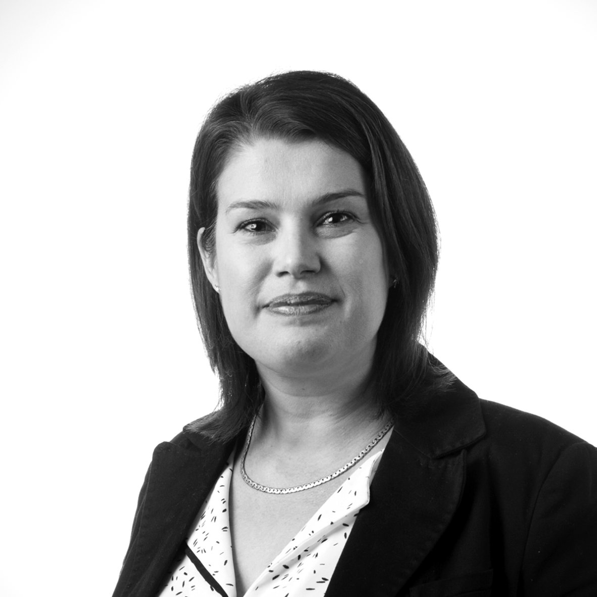 Femme souriante en portrait professionnel noir et blanc, cheveux mi-longs, veste sombre et collier fin.